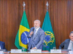 Lula falando em microfone e sorrindo, em pé