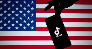 Mão segurando celular com logo do TikTok com bandeira dos EUA ao fundo